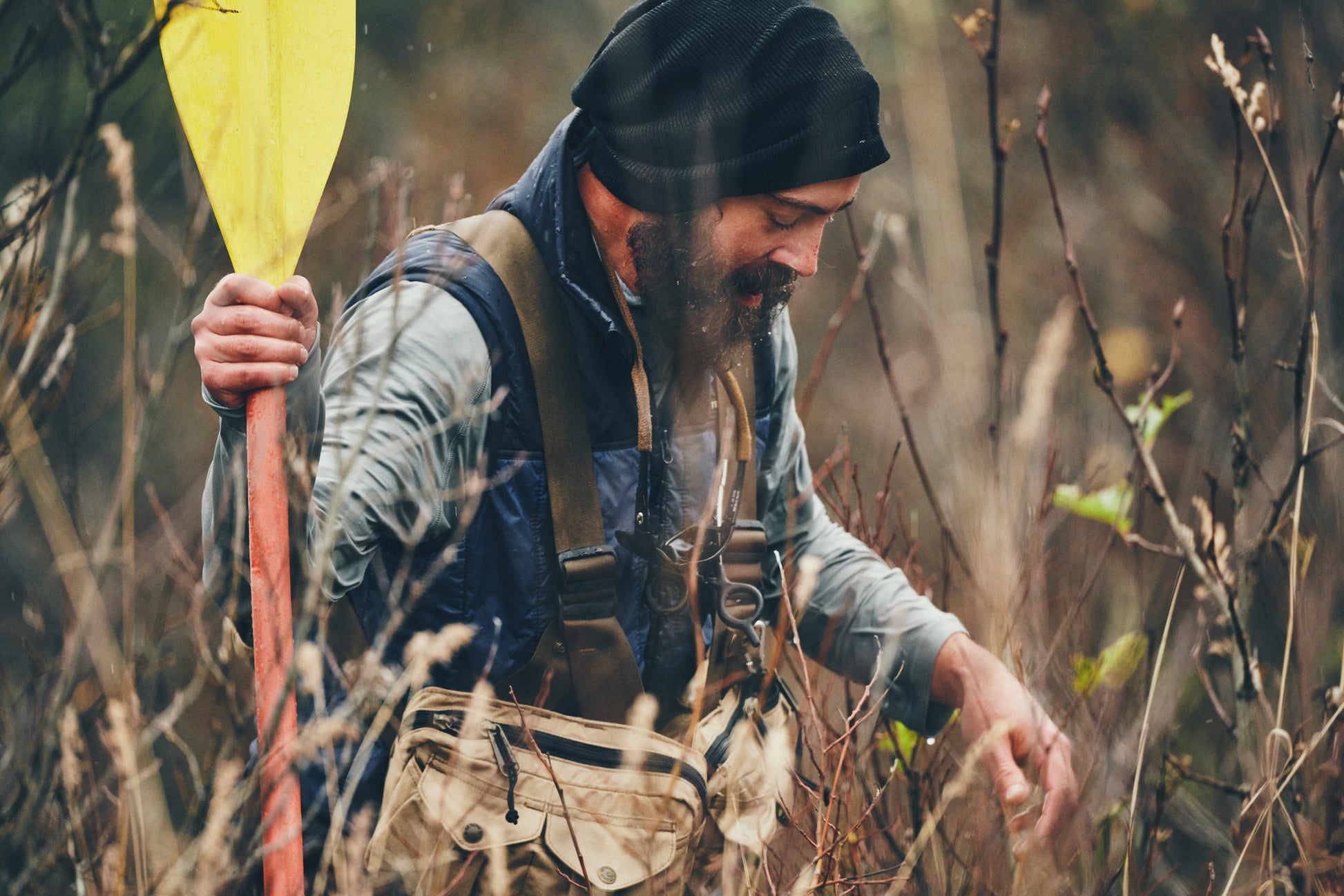 Man wearing Filson Mesh Fishing Strap Vest in dark tan walking through brush